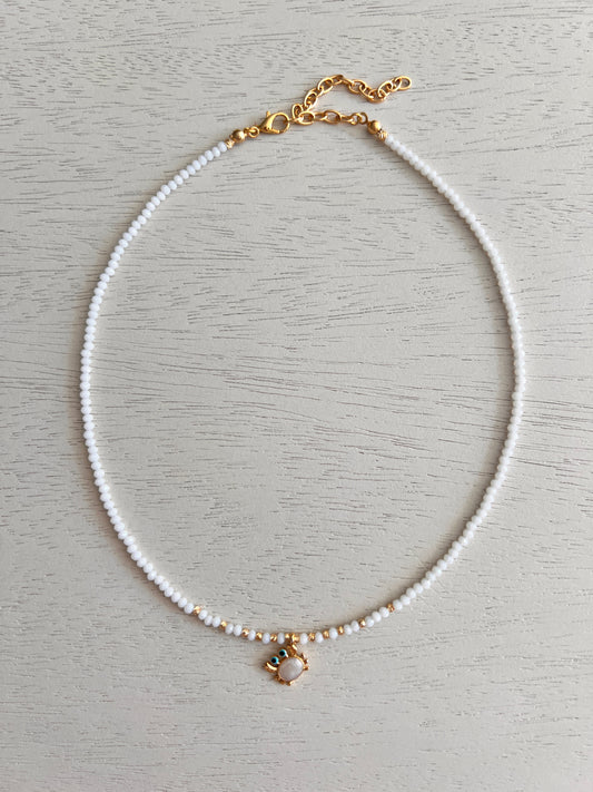White bead necklace with gold-plated enamel crab charm and blue details