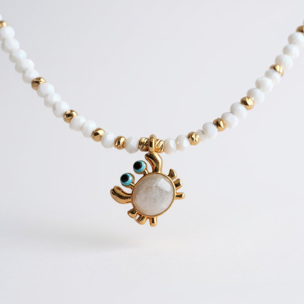 White bead necklace with gold-plated enamel crab charm and blue details