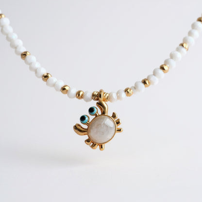 White bead necklace with gold-plated enamel crab charm and blue details