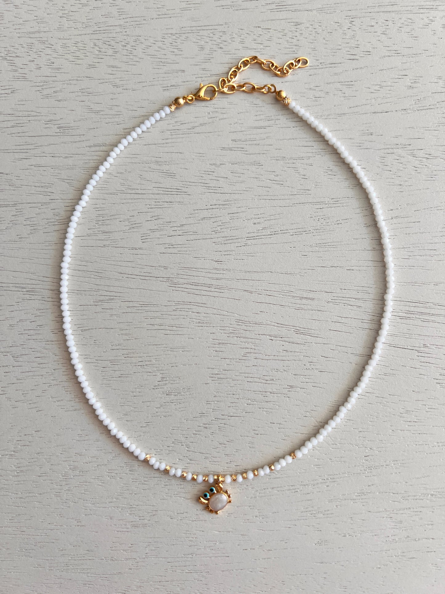 White bead necklace with gold-plated enamel crab charm and blue details